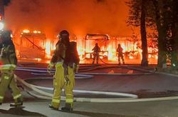 Na zdjęciu płonące autobusy, przy nich strażacy.