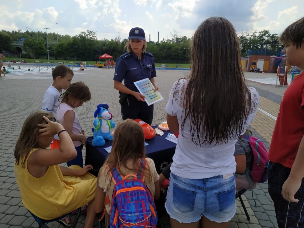 Zdjęcie kolorowe: umundurowana policjantka i policjant katowickiej komendy podczas spotkania z dziećmi i ich opiekunami na kąpielisku miejskim "Bugla" w Katowicach