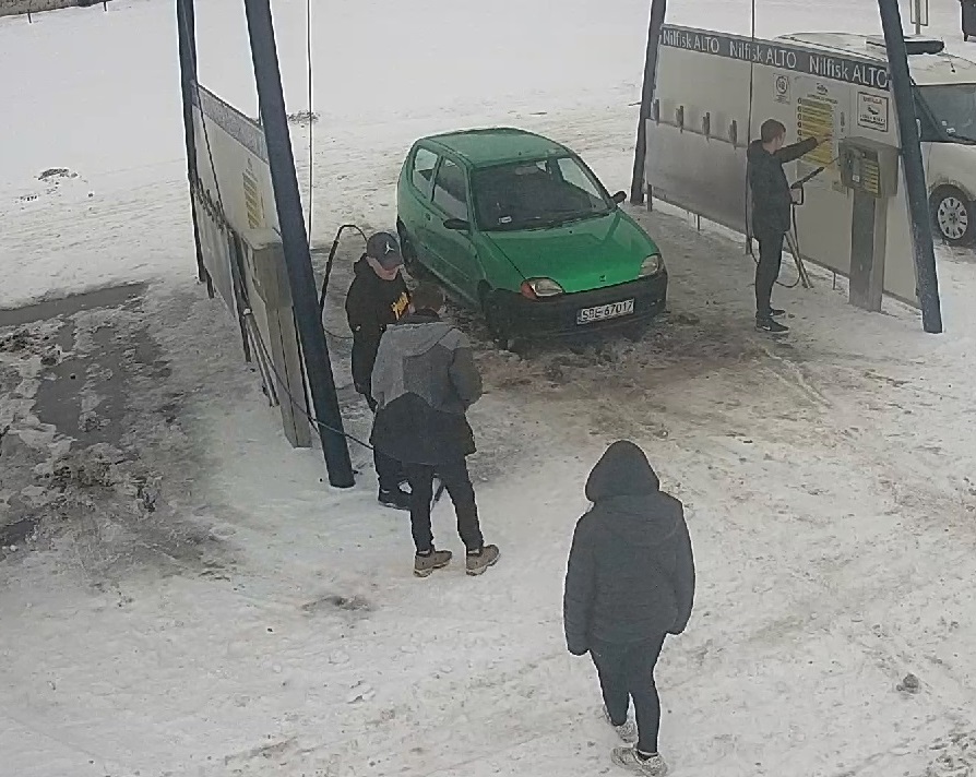 zdjęcie kolorowe: teren myjni samochodowej, zaparkowany zielony samochód osobowy i trzech mężczyzn podejrzewanych o jej zniszczenie  oraz świadek