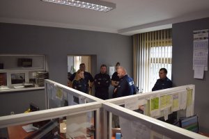 policjanci z Niemiec stoją na stanowisku dowodzenia dyżurnego a polscy policjanci opowiadają im o pracy dyżurnych