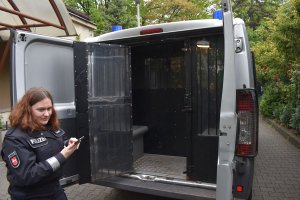 Niemiecka policjantka stoi za radiowozem w radiowozie są otwarte tylne drzwi od przedziału dla osób zatrzymanych