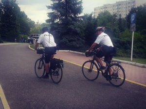 Na zdjęciu widać dwóch policjantów jadących na rowerach za nim są drzewa