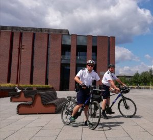 Na zdjęciu widać dwóch policjantów na rowerach za nim stoi budynek narodowej orkiestry symfonicznej polskiego radia