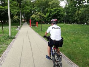 Na zdjęciu widać policjanta na rowerze jadącego przez park