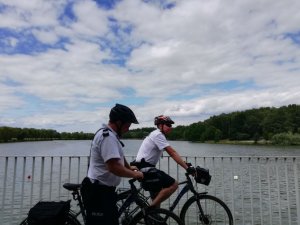 Na zdjęciu widać dwóch policjantów na rowerach za nim jest jezioro