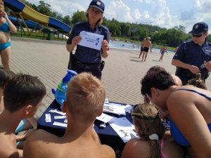 Zdjęcie kolorowe: umundurowana policjantka i policjant katowickiej komendy podczas spotkania z dziećmi i ich opiekunami na kąpielisku miejskim &amp;quot;Bugla&amp;quot; w Katowicach