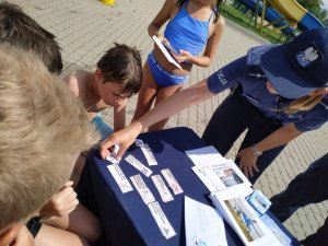 Zdjęcie kolorowe: umundurowana policjantka i policjant katowickiej komendy podczas spotkania z dziećmi i ich opiekunami na kąpielisku miejskim &quot;Bugla&quot; w Katowicach