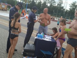 Zdjęcie kolorowe: umundurowana policjantka i policjant katowickiej komendy podczas spotkania z dziećmi i ich opiekunami na kąpielisku miejskim &quot;Bugla&quot; w Katowicach