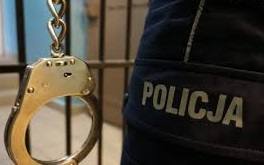 zdjęcie kolorowe: kajdanki na tle kraty aresztu i napisu Policja