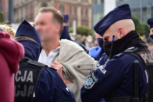 zdjęcie kolorowe: dwóch katowickich policjantów podczas czynności legitymowania wobec mężczyzny nie stosującego środków ochrony osobistej